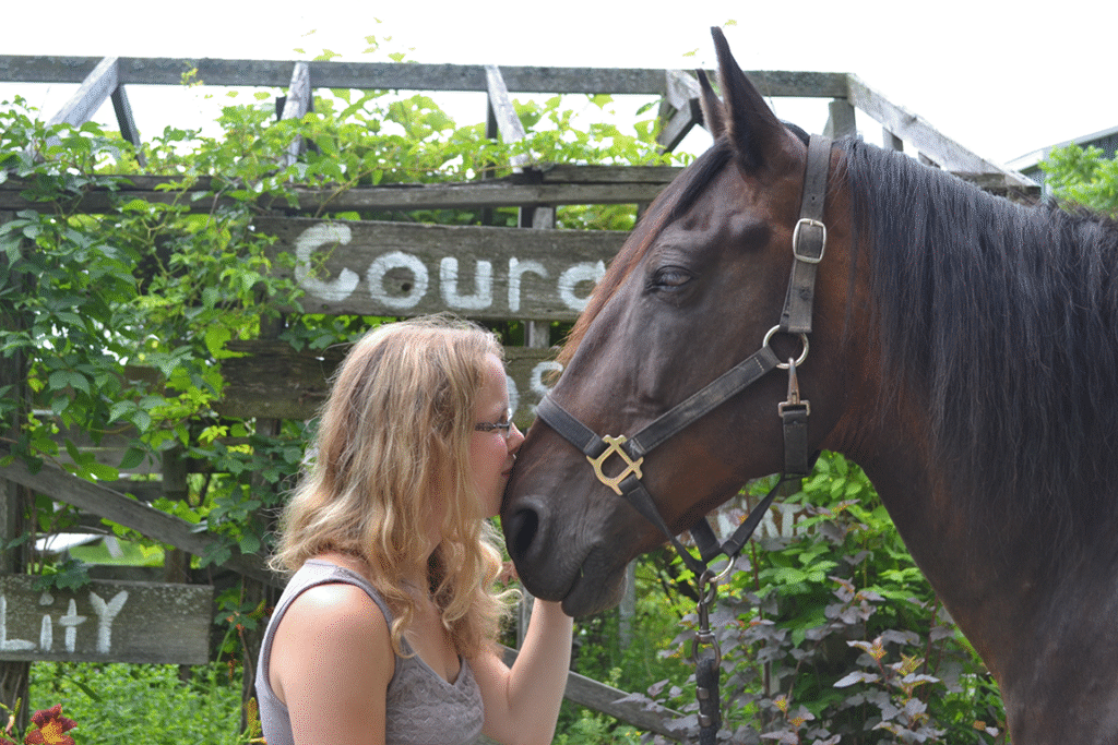 woman gently kisses the nose of a horse