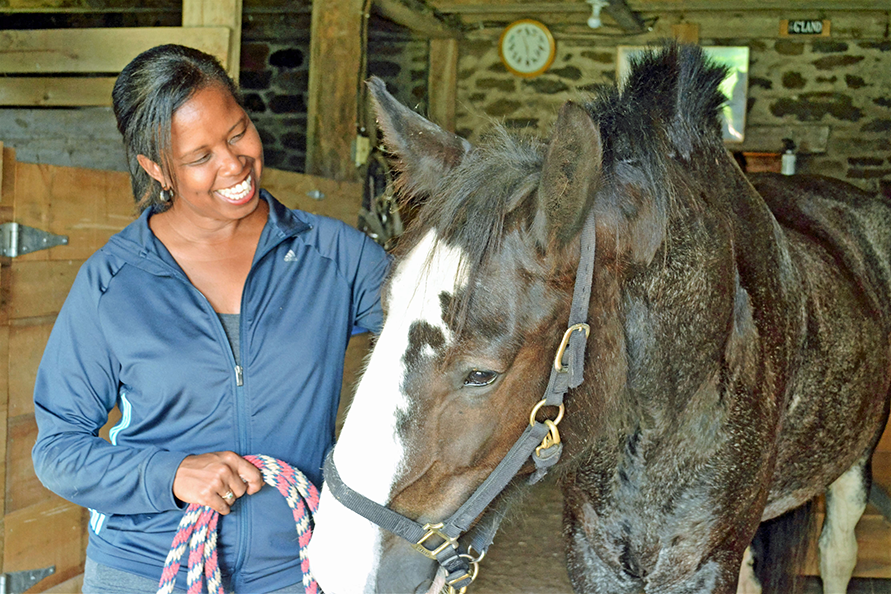 woman smiles lovingly at horse as they duck their head slightly