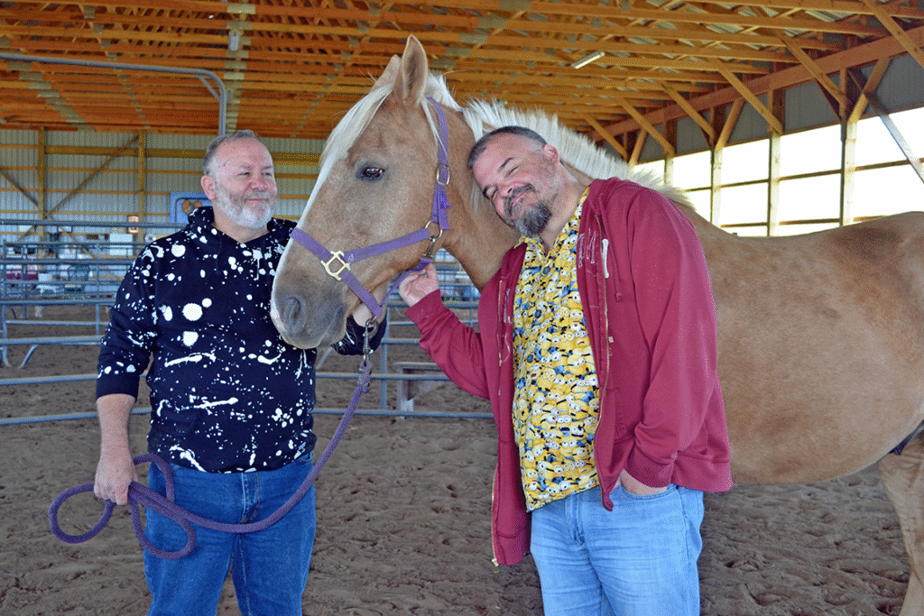 Two men stand beside a horse, looks of love and contentment on their faces.