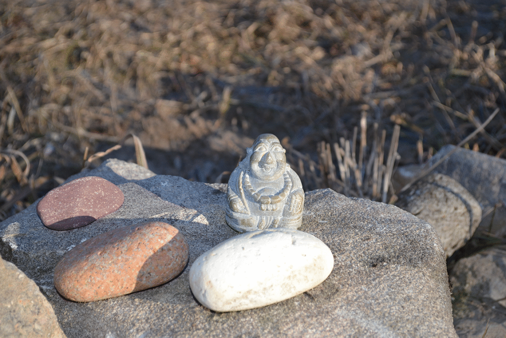 buddha statue sitting next to three small stones on a larger boulder